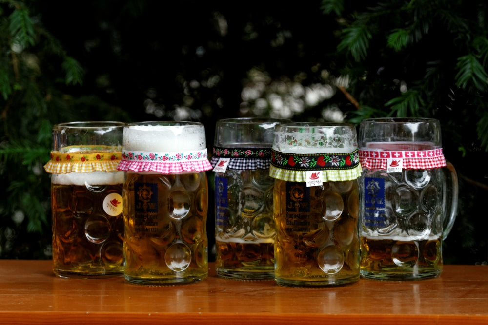 Fünf Maßkrüge stehen auf einer Bierbank und jeder Maßkrug ist verziert mit einem Maßkrugband by vronikaa