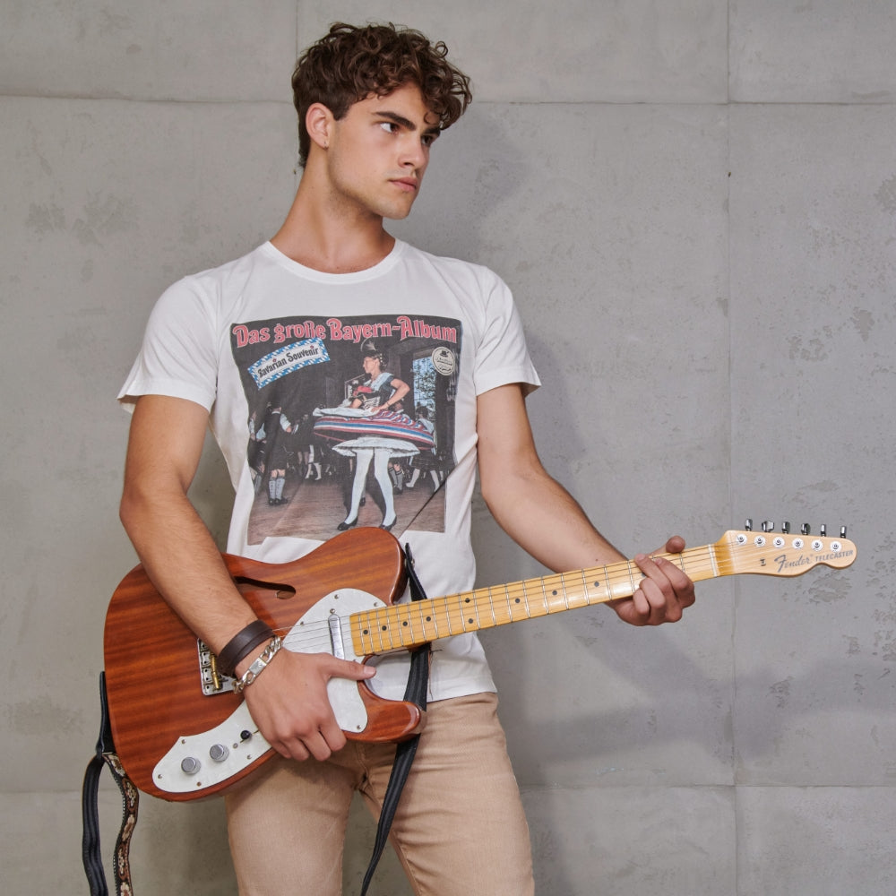 Mann spielt Rock Gitarre vor einer Betonwand uns trägt ein Shirt mit dem Aufdruck "Das große Bayern Album"