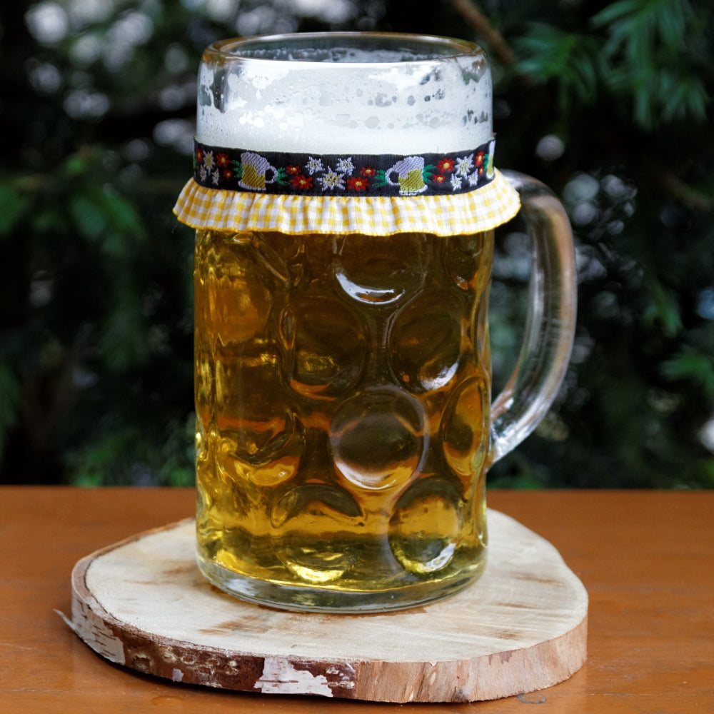 Ein mit Bier gefüllter Maßkrug mit Maßkrugband in Gelb mit Bierkrügen und Edelweiß