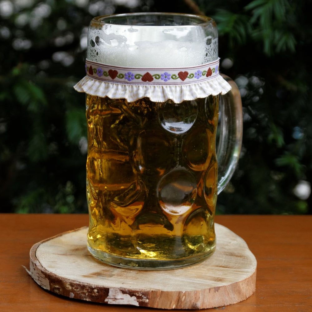 Ein mit Bier gefüllter Maßkrug mit Maßkrugband in Beige kariert mit braunen Herzen und lila Blumen