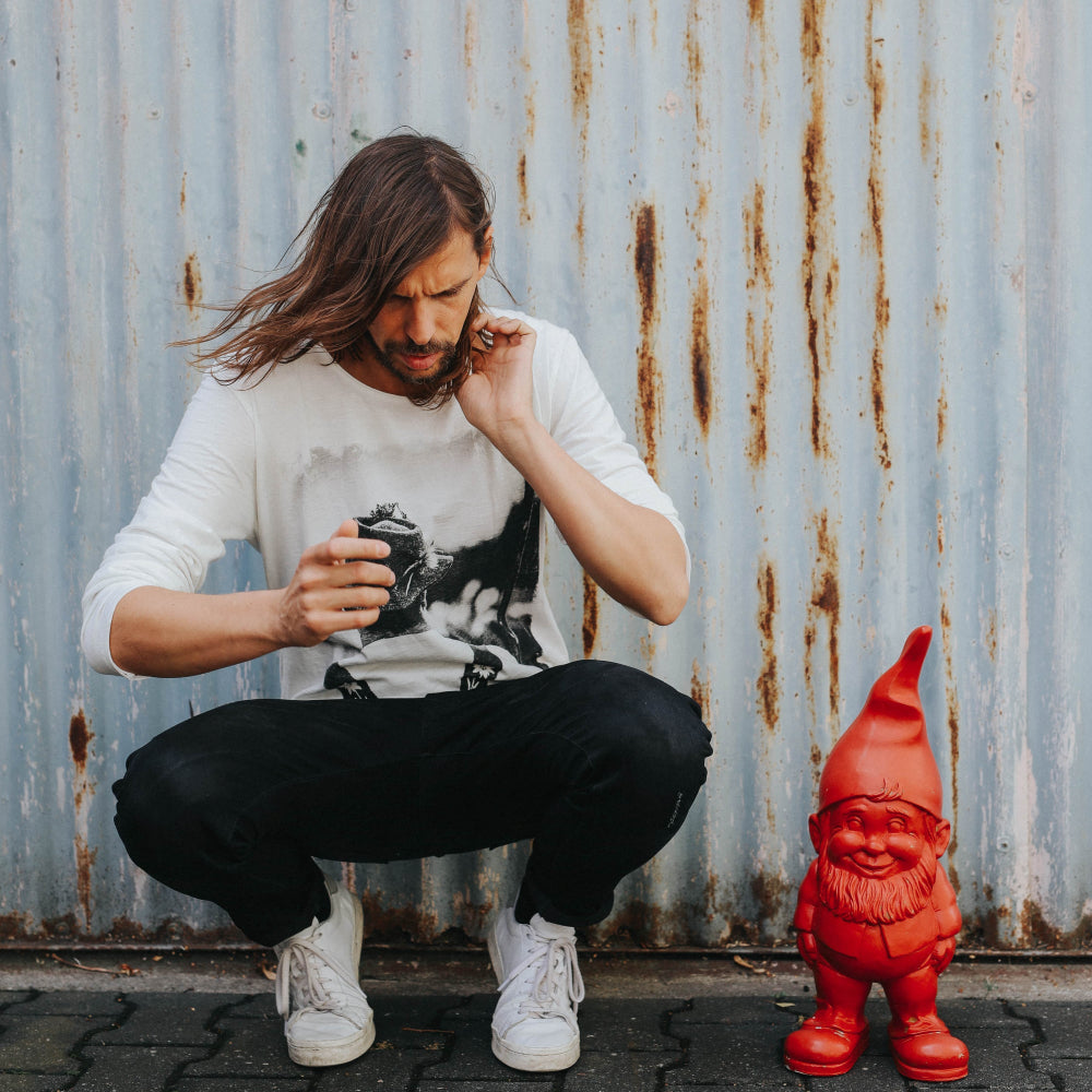 Model trägt das Longsleeve Hirte mit weißen Sneakers und ein roter Gartenzwerg steht im Bild. 