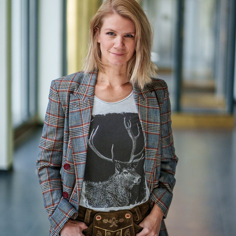 Model mit Bob Haarschnitt trägt das Shirt Hirschgeweih zur Damen-Lederhose und einen karierten Blazer darüber