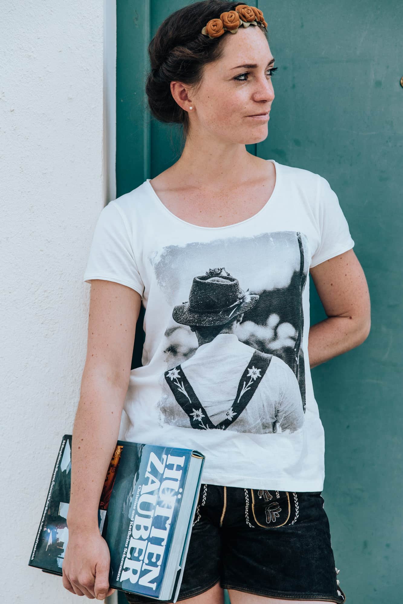 Model in Lederhose und dem Shirt Hirte hält ein Hütten Zauber Buch in der Hand.
