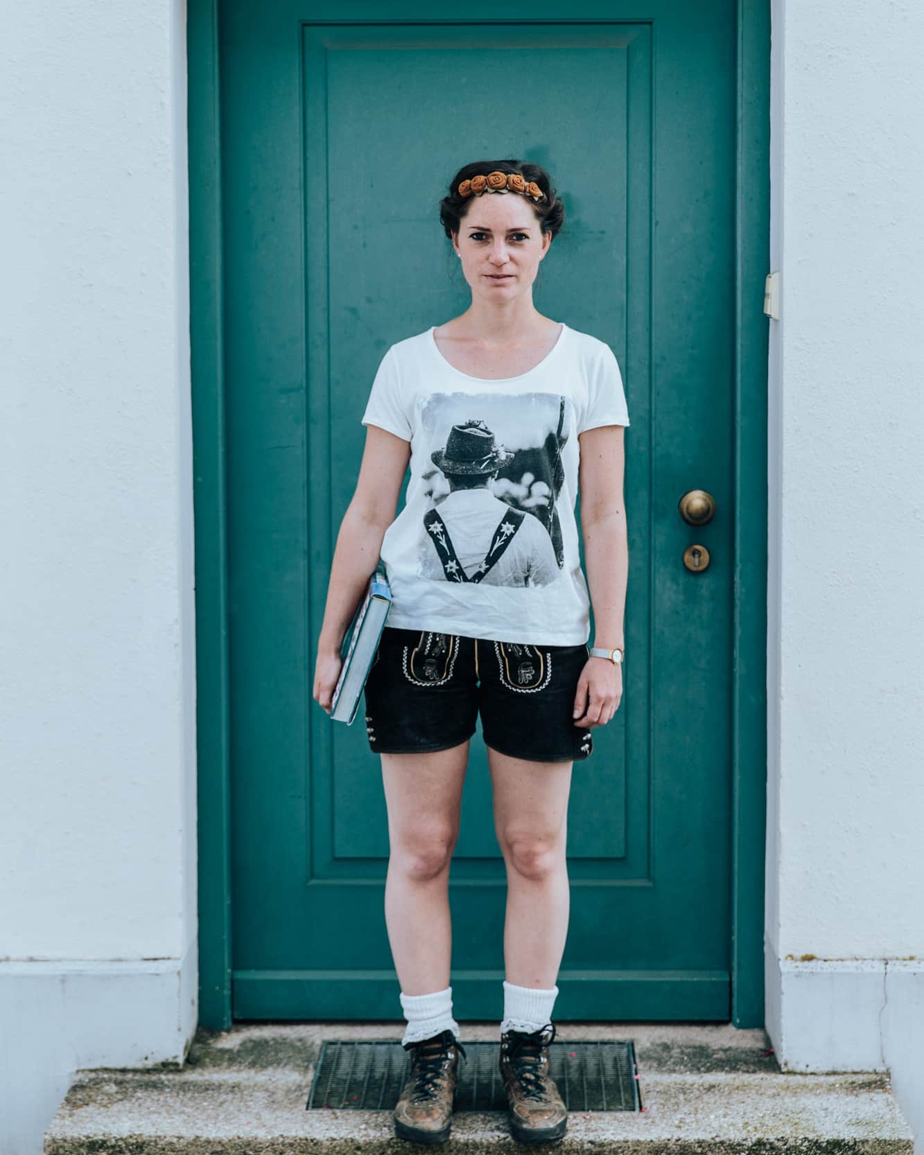 Model mit dem Shirt Hirte in der Farbe Offwhite vor einer Tür in Türkis. 