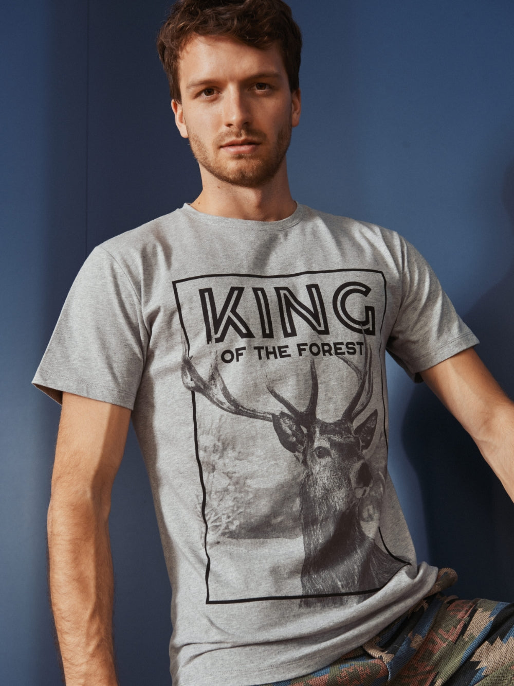 Model trägt ein graues Shirt mit großem Aufdruck eines Hirsches und dem Schriftzug King of the Forest