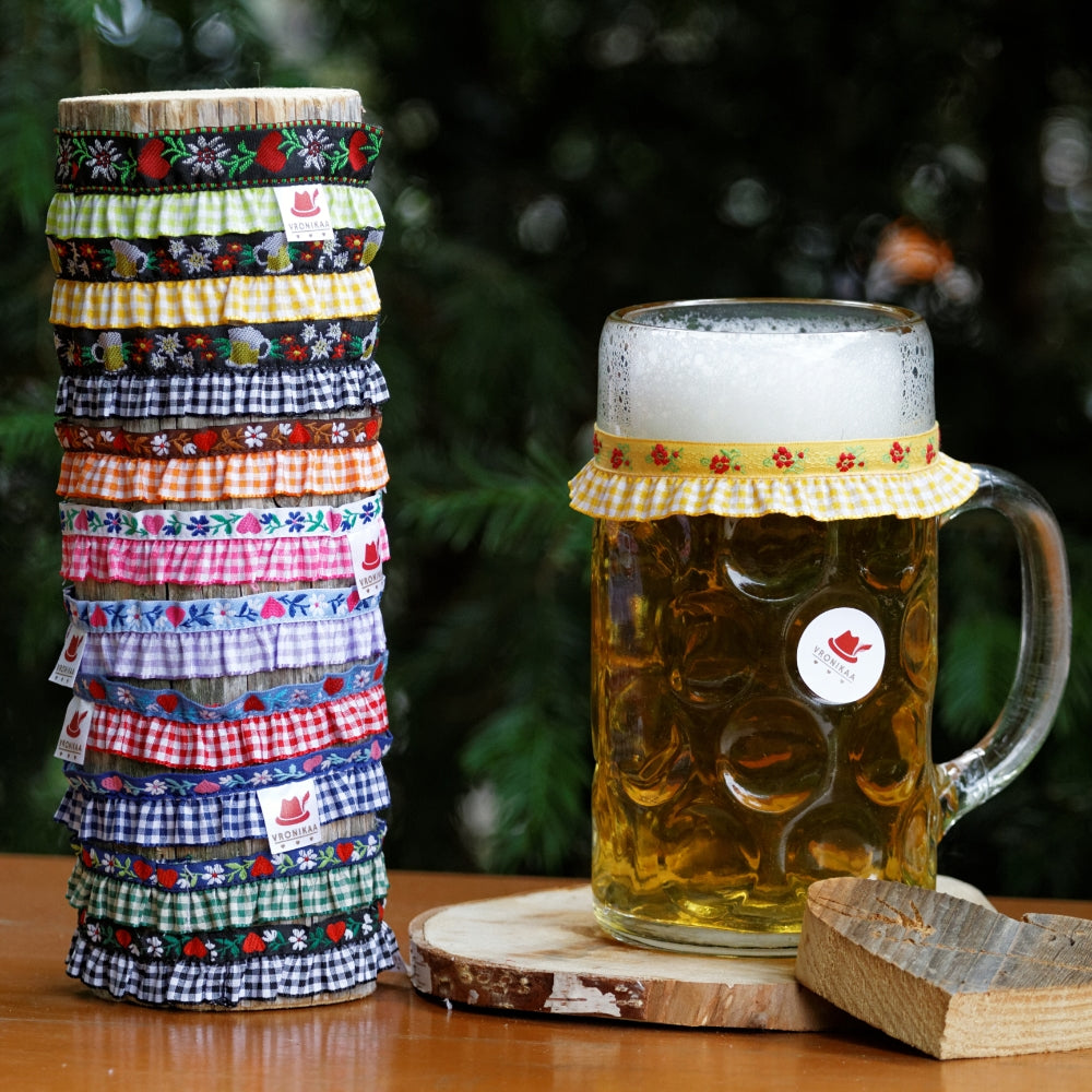 Ein Maßkrug mit frischen Bier gefüllt steht auf einem Biertisch, daneben steht ein Holzpflock mit einer Auswahl an verschieden farbigen Maßkrugbändern by vronikaa
