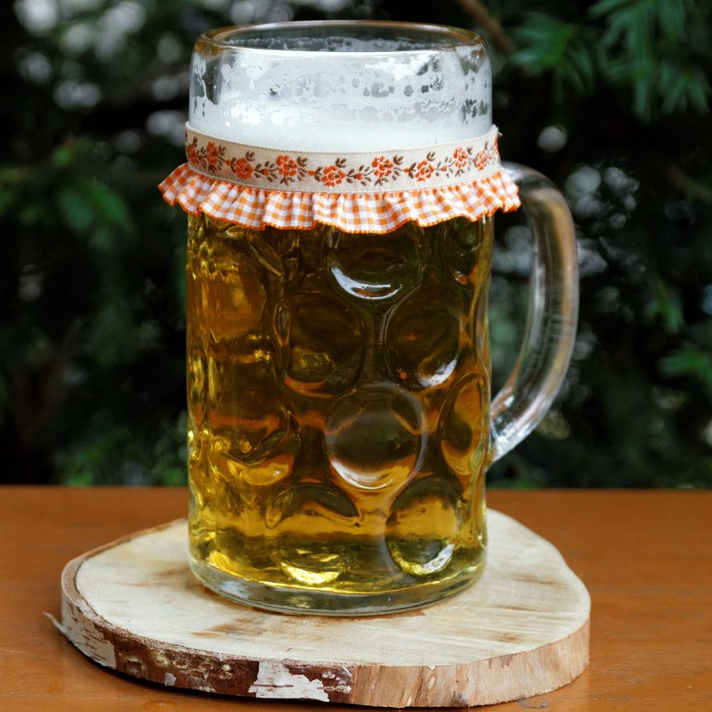 Ein mit Bier gefüllter Maßkrug mit Maßkrugband in Orange kariert mit Blumen