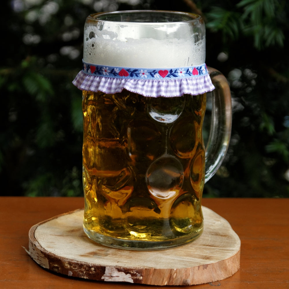 Ein mit Bier gefüllter Maßkrug mit Maßkrugband in Lila kariert mit rosa Herzen
